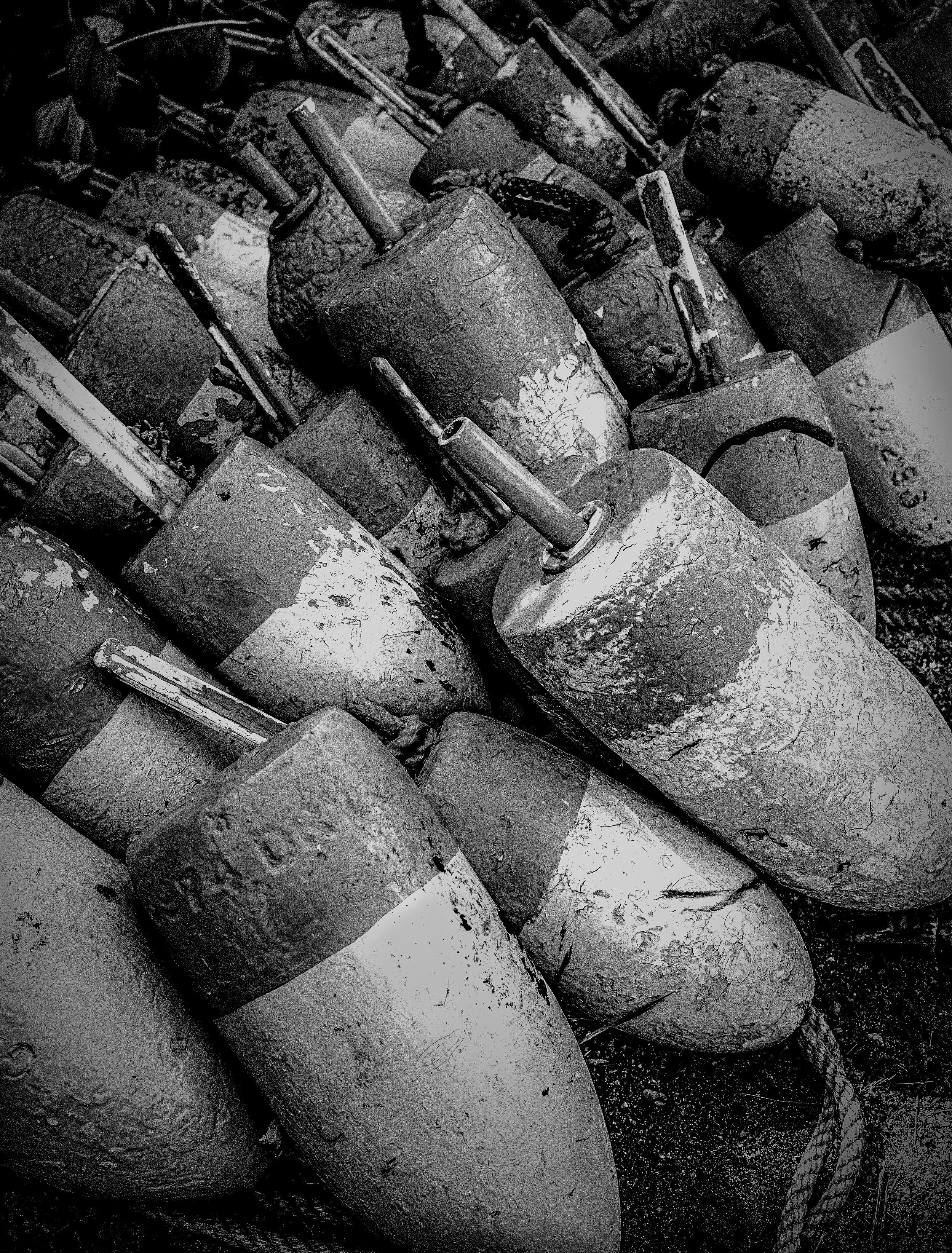 A pile of rusty, weathered bombs stacked haphazardly, with some showing signs of corrosion and chipped paint, and a thick rope lying on the ground among them.