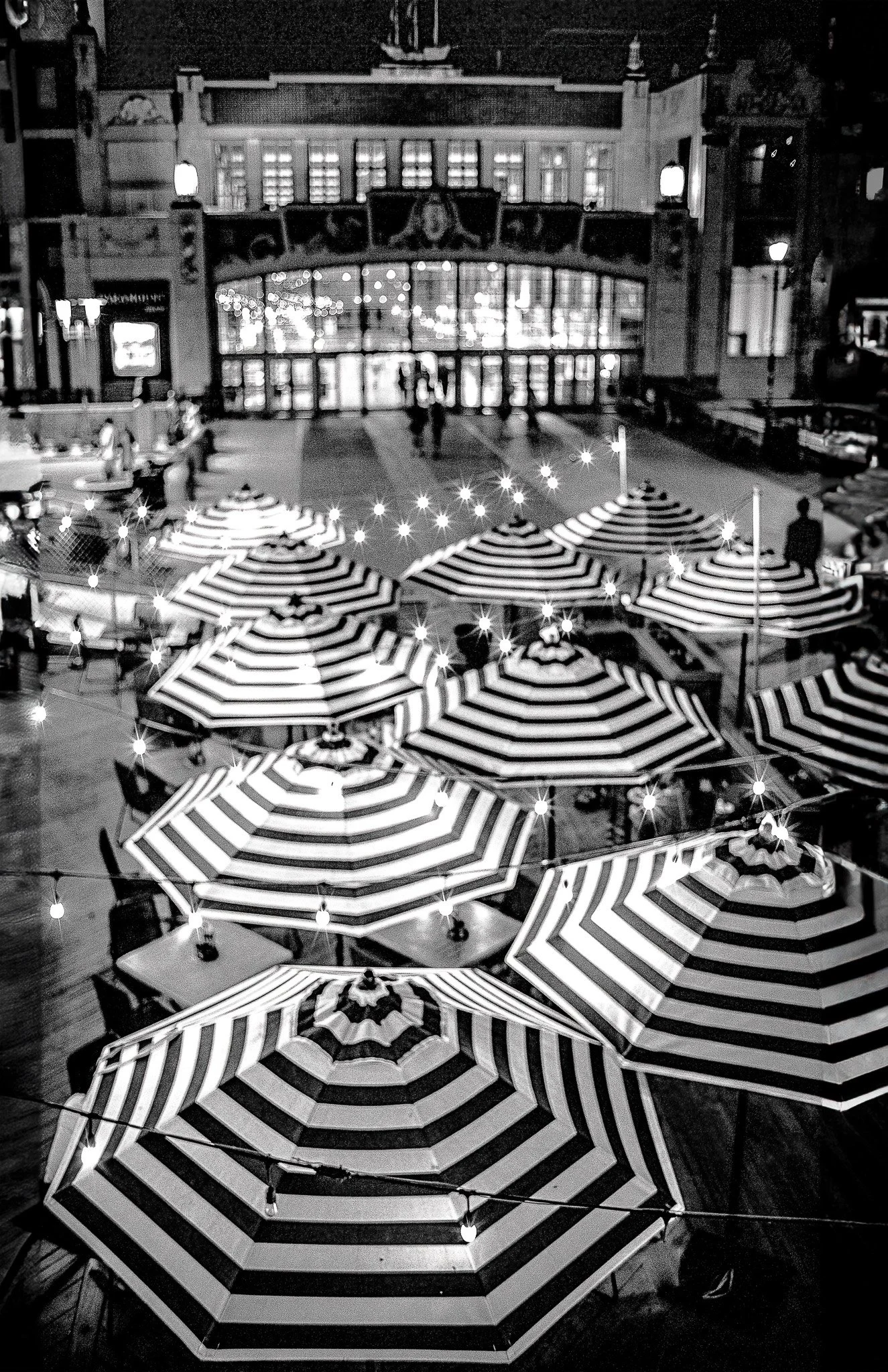 Nighttime scene showing a city street with multiple closed striped umbrellas and string lights hanging above, with a building in the background.