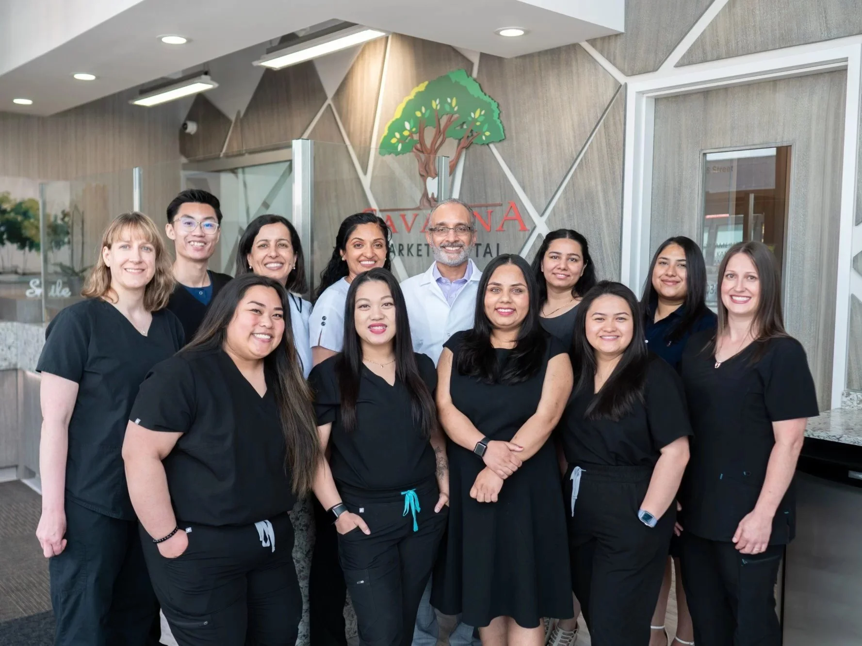 Group of ten diverse healthcare workers in scrubs posing together in front of a sign that reads