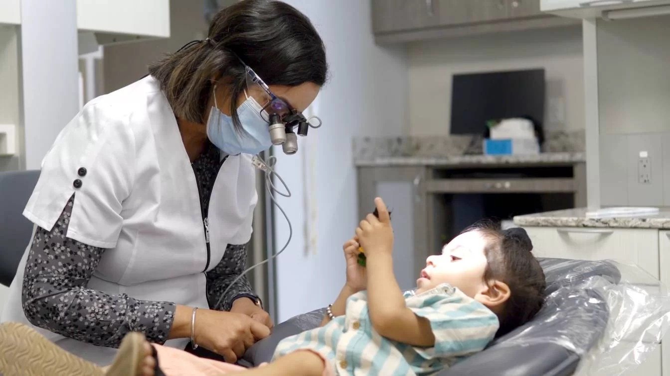 A female doctor wearing a face mask and headlamp examines a young girl lying in a medical clinic.