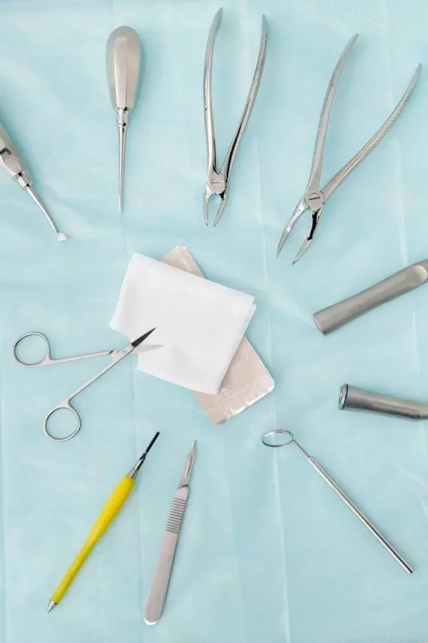 Collection of dental tools, including forceps, scissors, a scaler, and other instruments, arranged on a light blue surface, likely in a dental setting.