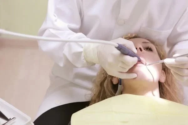 A dentist is performing a dental procedure on a patient lying in a dental chair, with the patient wearing a yellow bib.