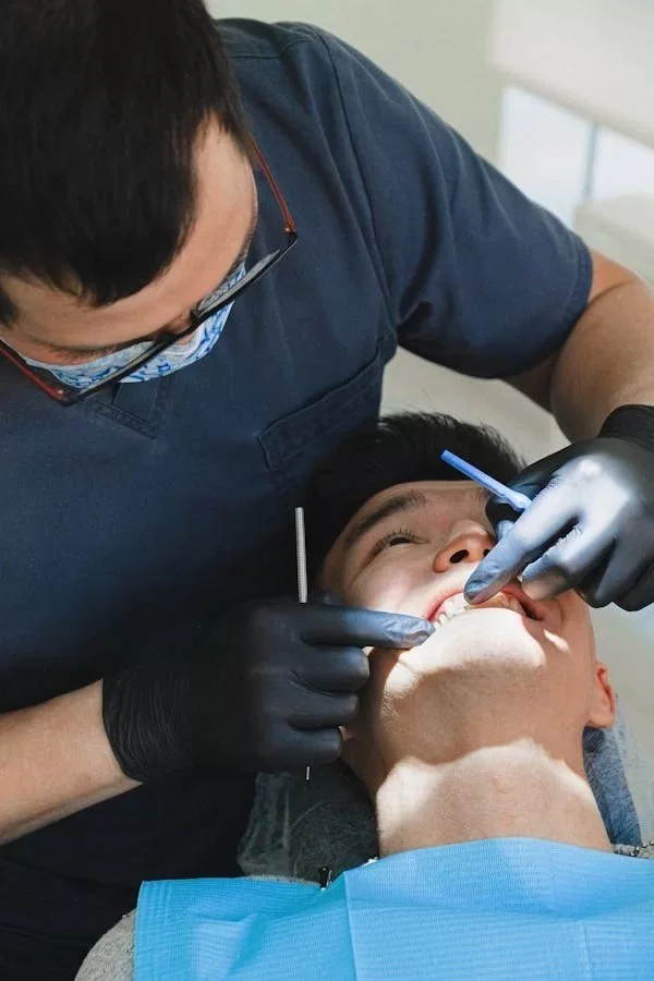 Dentist in black gloves examining a male patient in a dental chair.