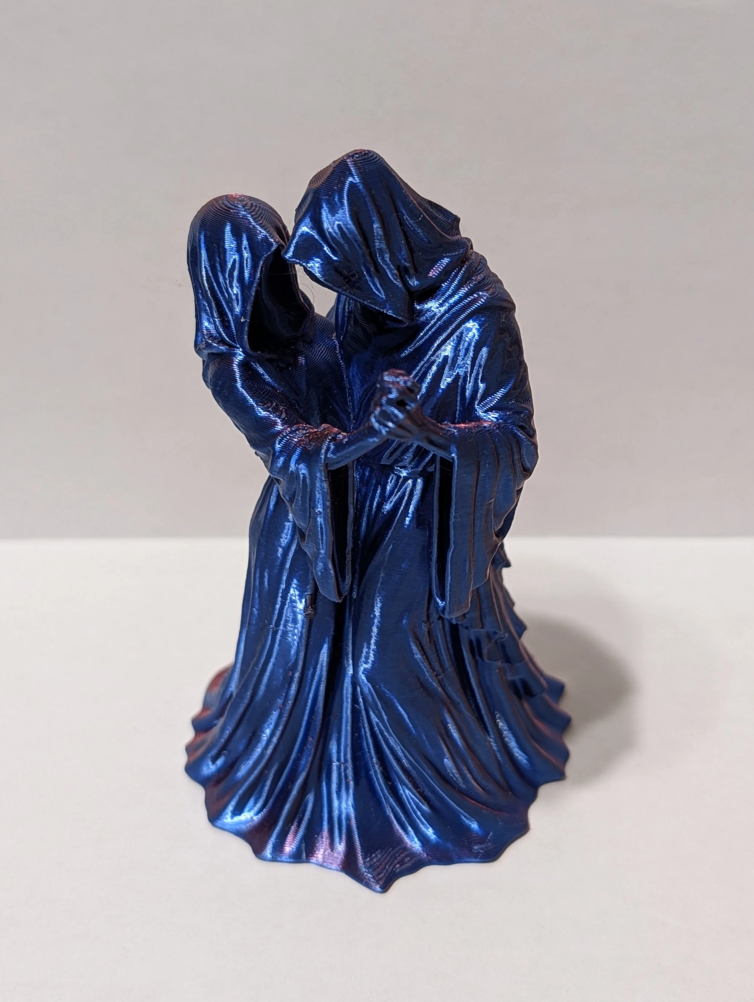 A metallic blue figure with a flowing, pleated skirt and matching hooded top, standing against a plain light-colored background.