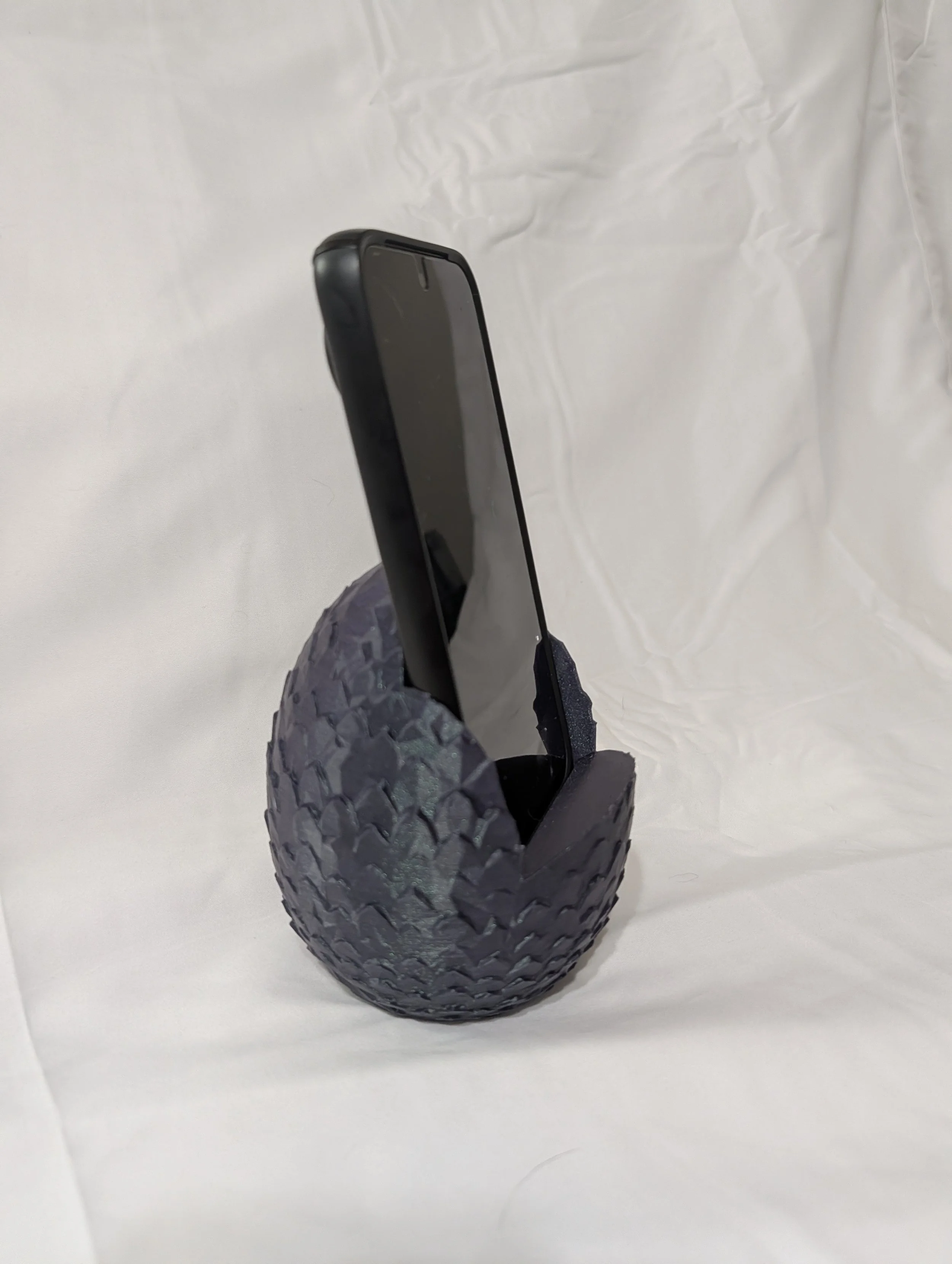 A smartphone resting on a textured black rubber tire-shaped holder against a plain white background.