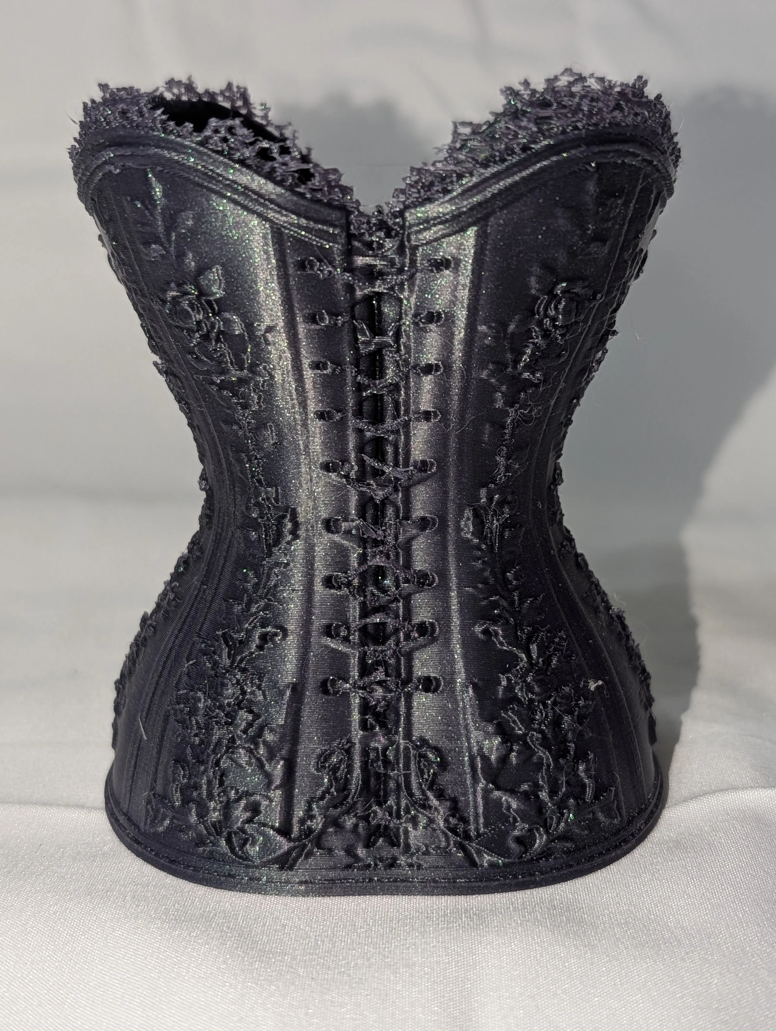 A black corset with intricate embroidery, lace-up front, and shiny, textured fabric displayed on a white surface.