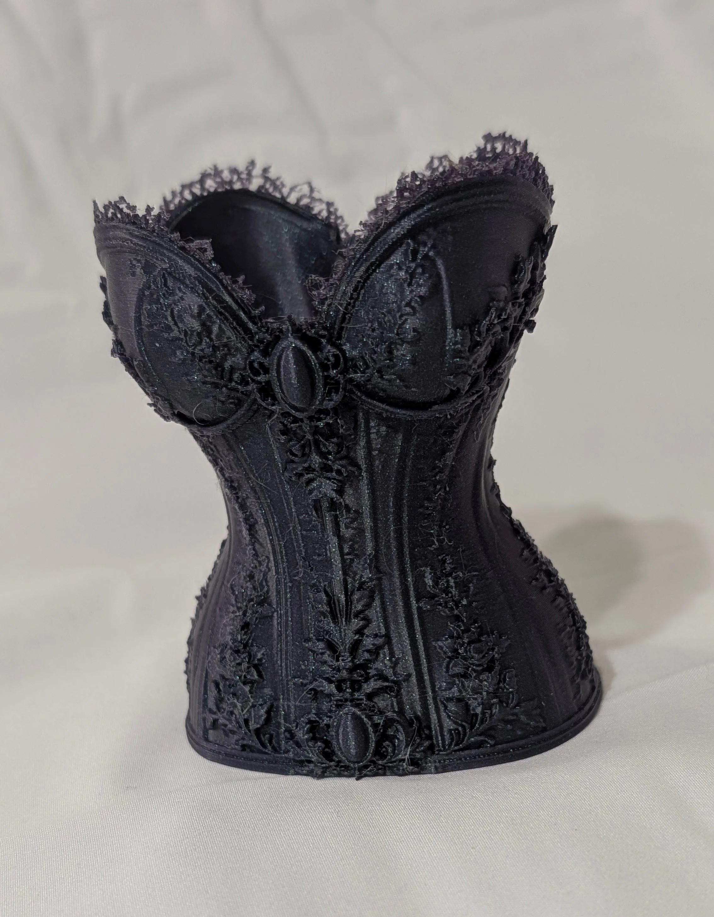 A black lace corset with intricate floral embroidery and lace trim, standing upright on a white surface.
