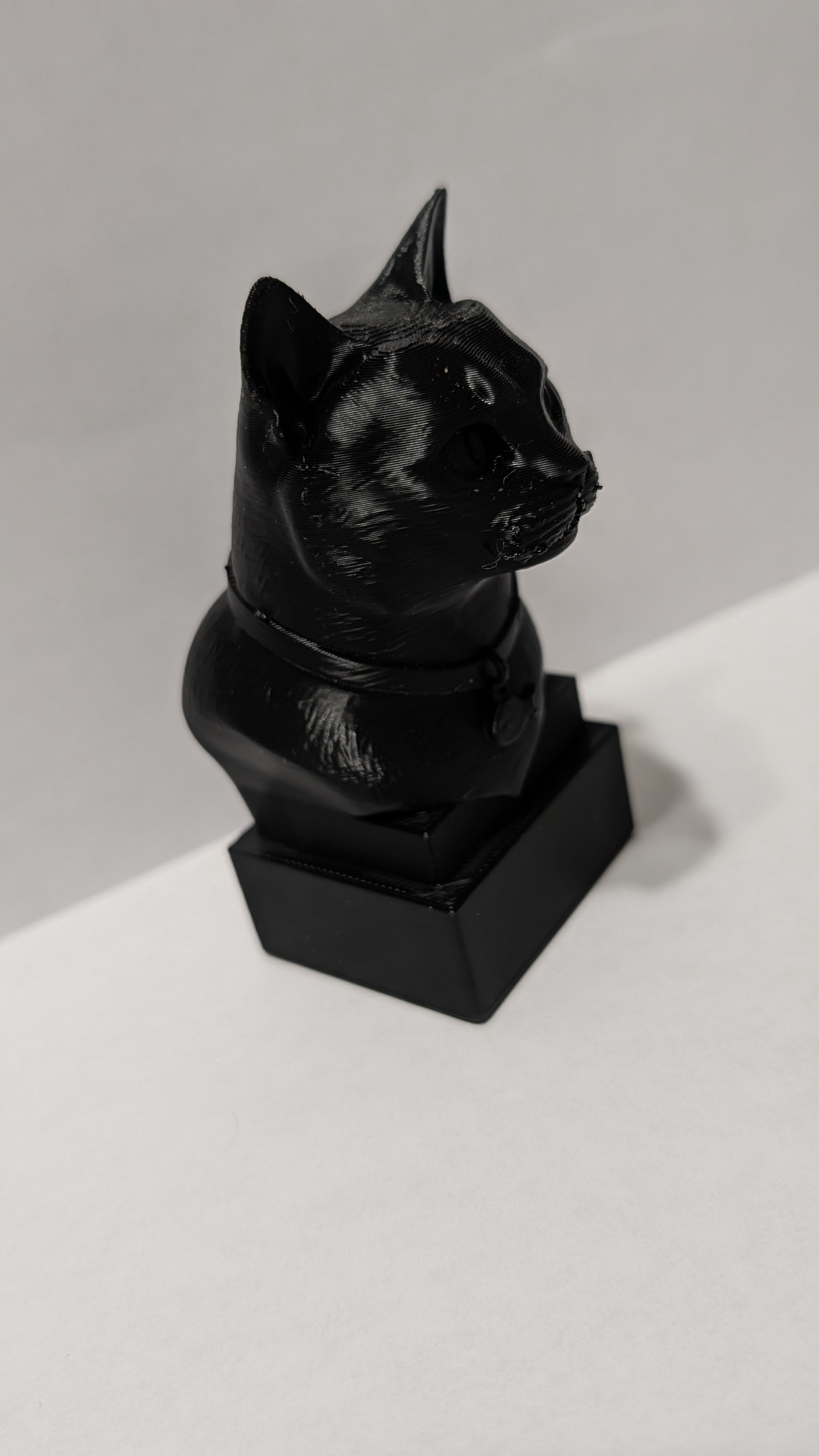 Black sculpture of a cat head on a black pedestal against a plain white background.