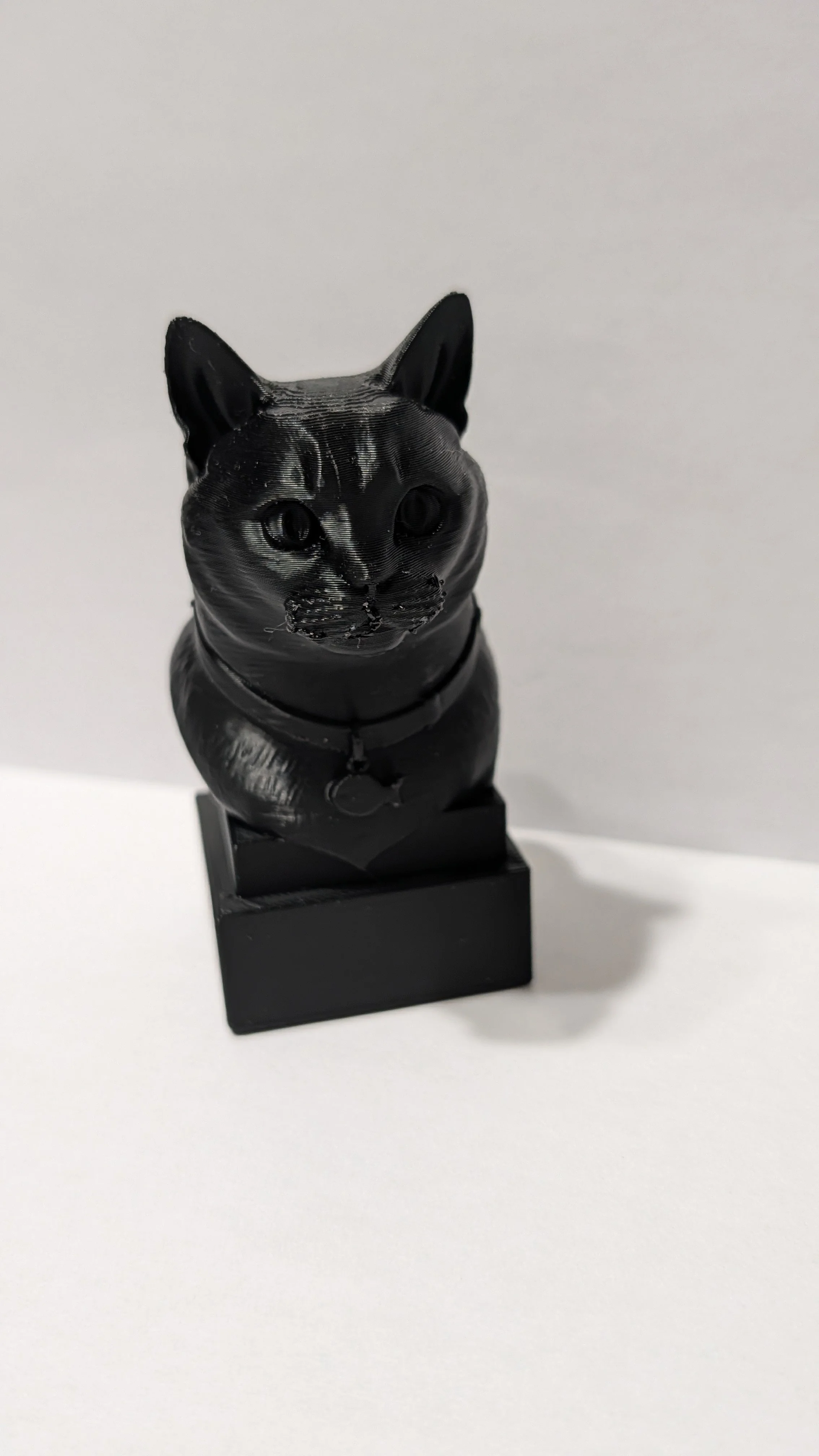 Black sculpture of a cat sitting on a black base against a plain background.