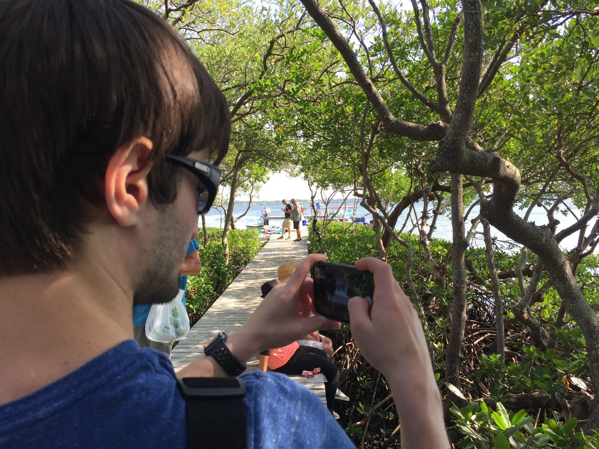 Ocean Fitts taking a photo on a mangrove-lined boardwalk leading to the water