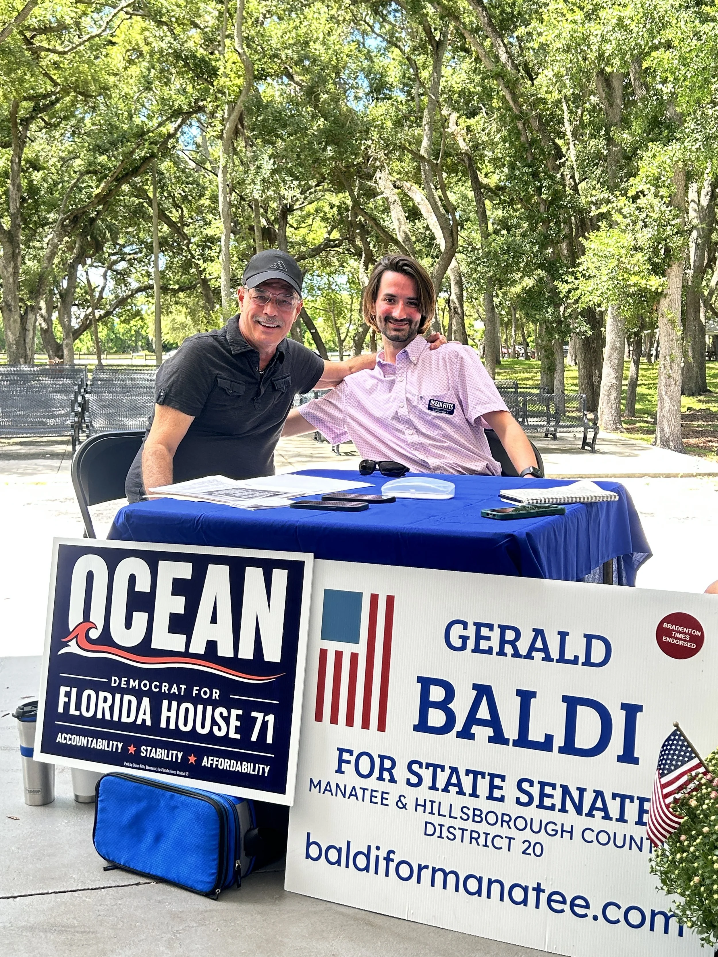 Ocean Fitts and Gerald Baldi, Democratic candidate for Florida Senate District 20, at a campaign table in a park