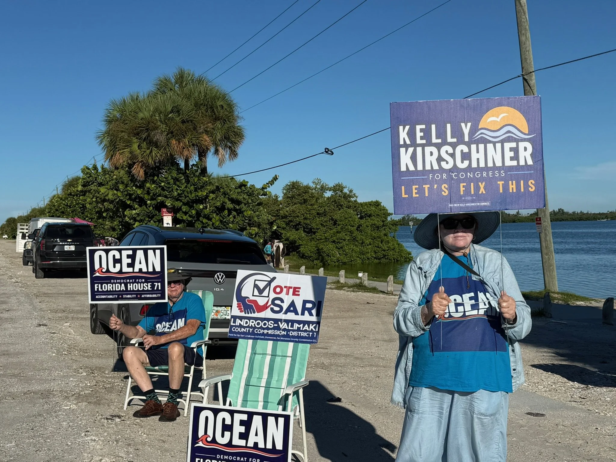 Volunteers holding Ocean Fitts for Florida House 71 and Sari Lindroos-Valimaki for County Commission District 1 signs by the water