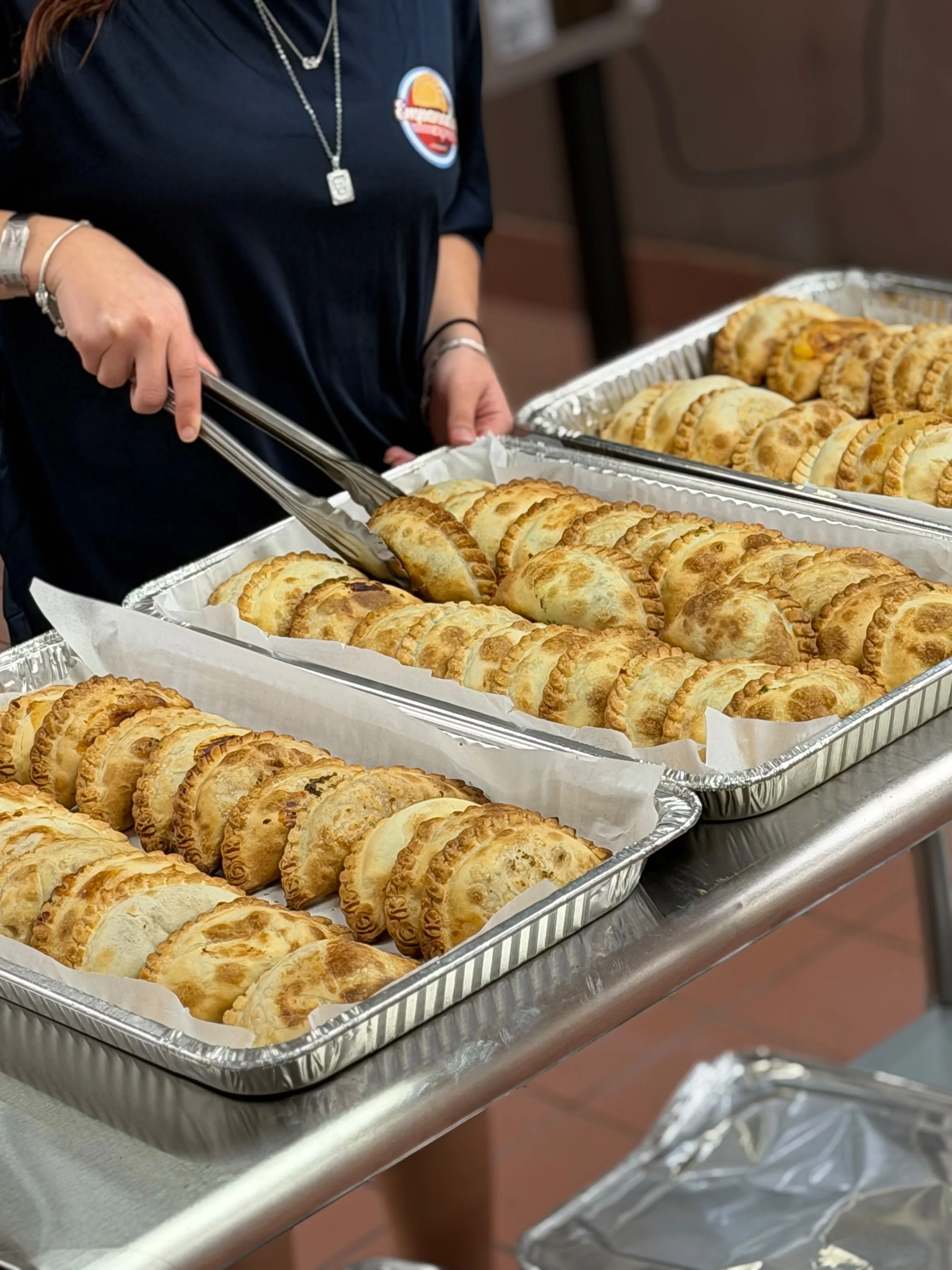 Empanadas Express team member using tongs to pick up an empanada from catering trays.
