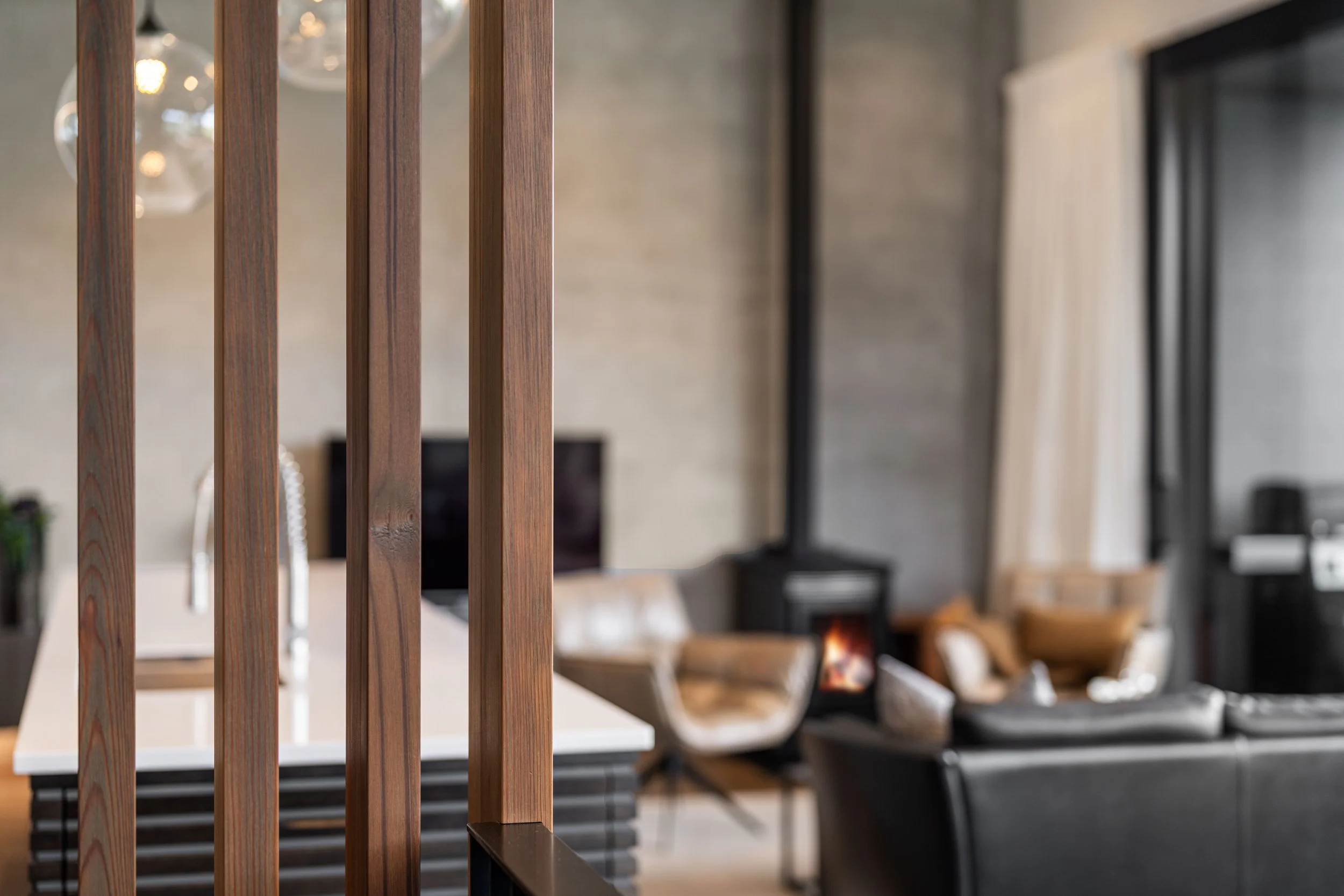Close-up of vertical wooden slats with a blurred interior background including a dining table and chairs, a fireplace, and a window.