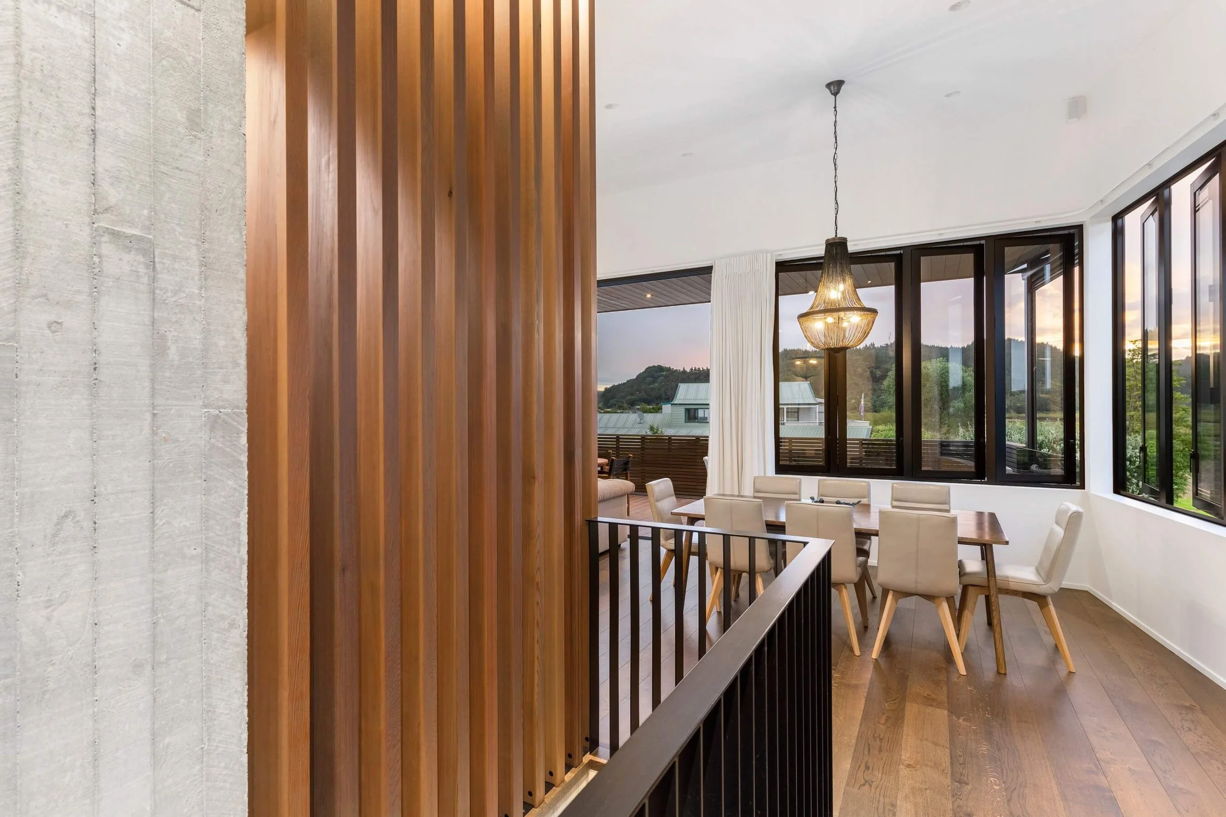 Interior view of a modern dining area with large windows, a wooden slatted room divider, and a hanging chandelier.
