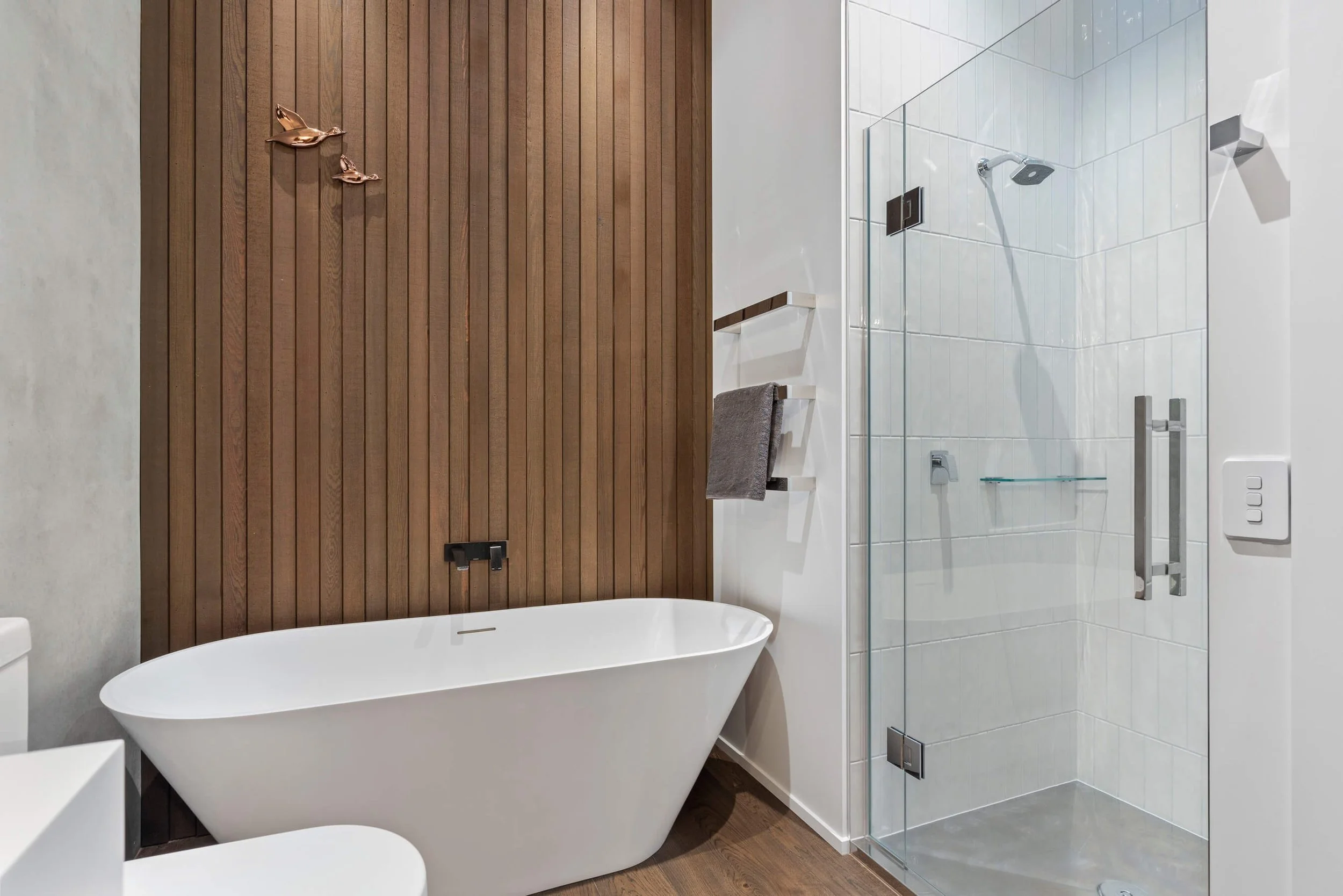 Modern bathroom with a freestanding bathtub, wooden accent wall, and a glass-enclosed shower with white tiled walls.