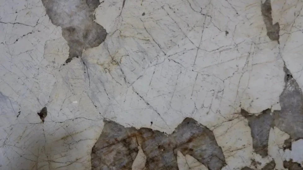 Close-up image of cracked, peeling white paint or plaster on a wall, revealing underlying darker, aged surface.