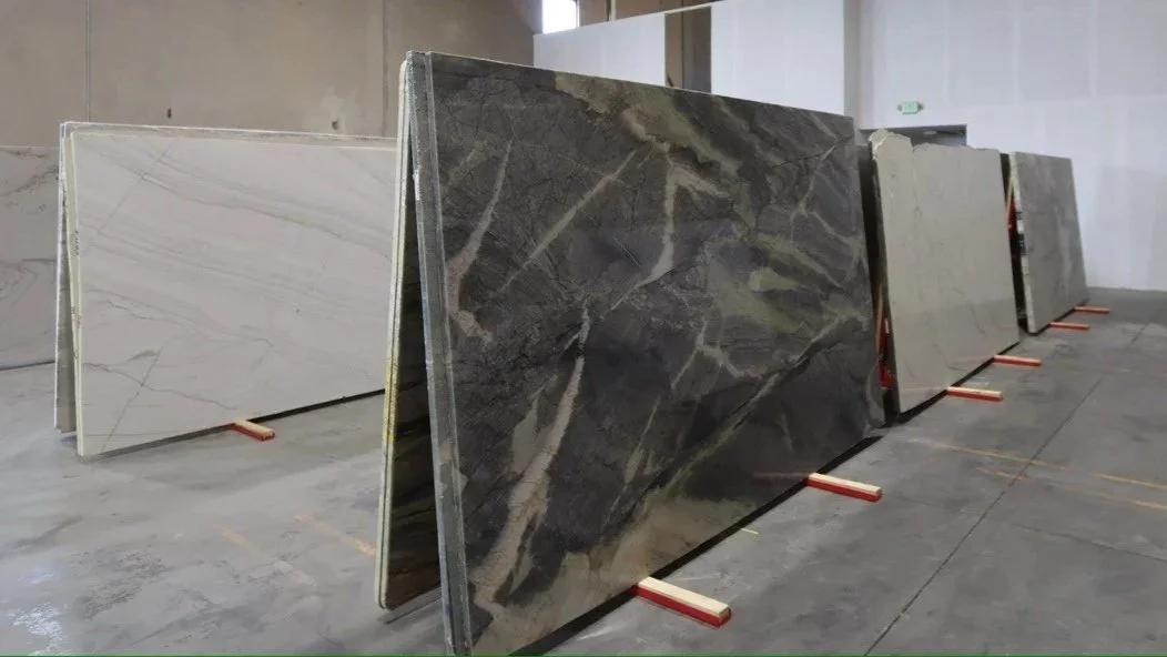 Large stone slabs with various marble and granite patterns standing vertically on wooden supports inside an industrial warehouse.