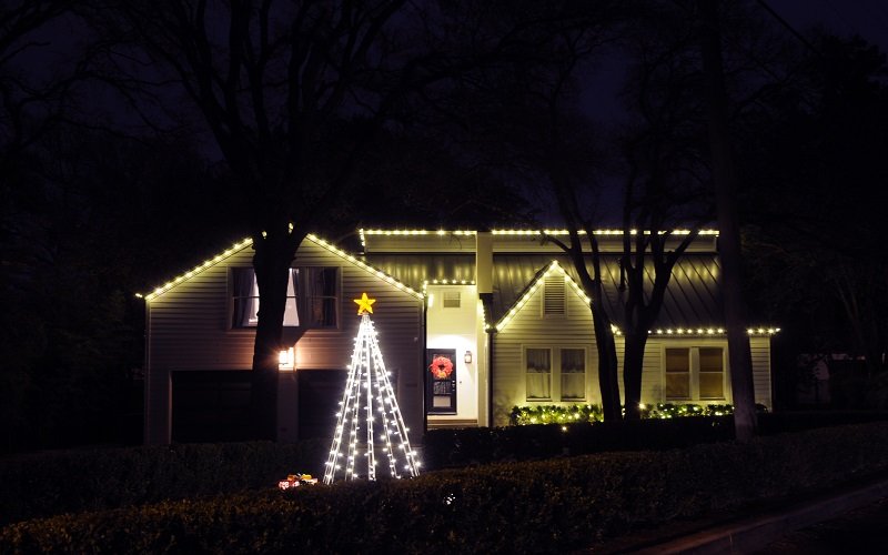 House decorated with Christmas lights, featuring a tree-shaped light display with a star on top and a wreath on the front door.