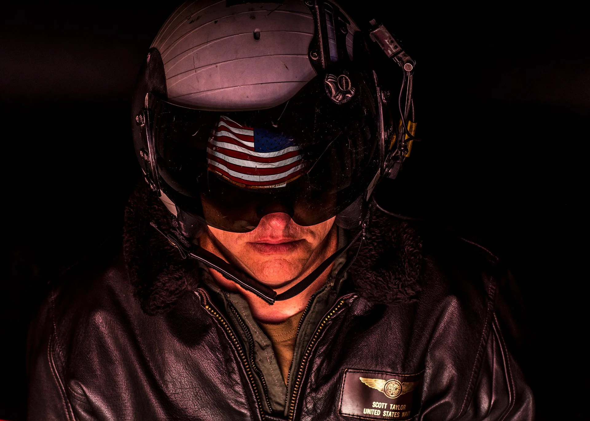 Fighter pilot against dark background with American flag reflected off closed visor.