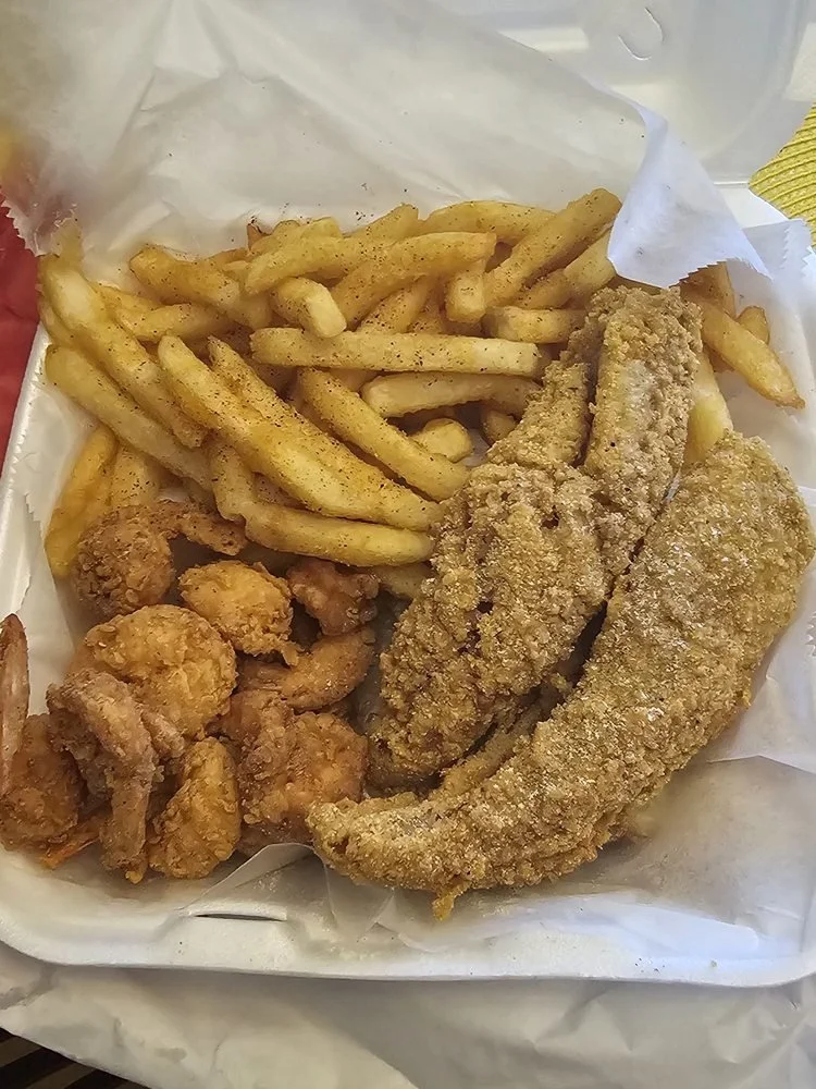 Fried fish fillets, French fries, and fried chicken pieces served on a paper-lined basket.