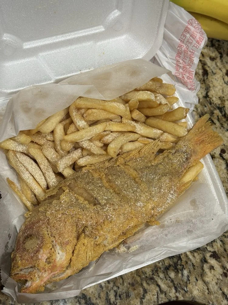 Fried fish with French fries in a takeout container on a granite countertop.