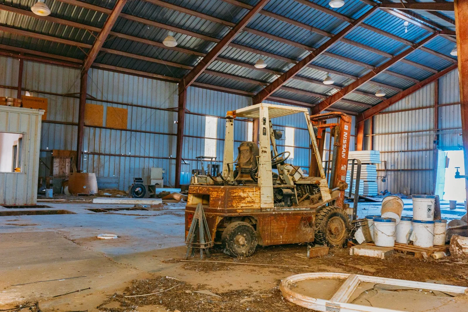 An empty industrial warehouse with a rusted forklift and scattered construction materials.