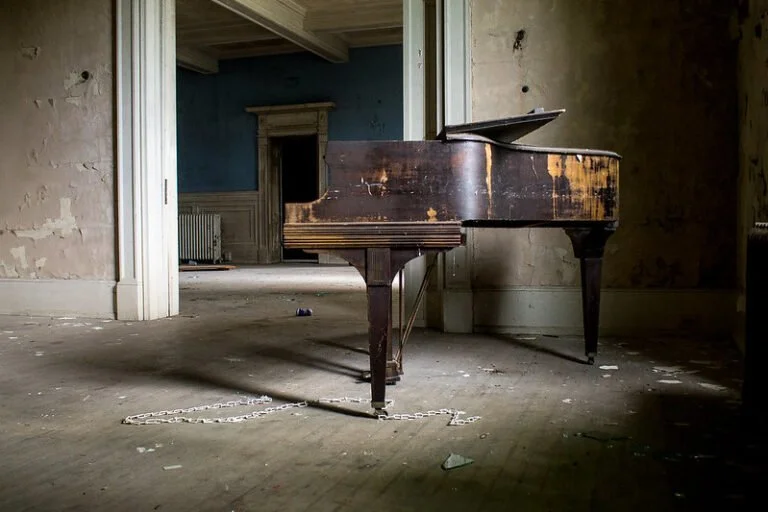 An old, worn-out grand piano in an abandoned room with peeling walls and dusty floors.