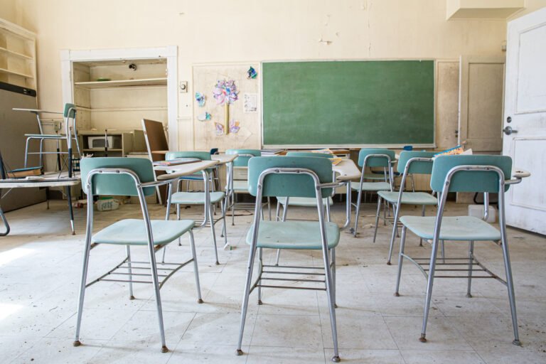 Empty classroom with blue chairs, a green chalkboard, and children's artwork on the wall.