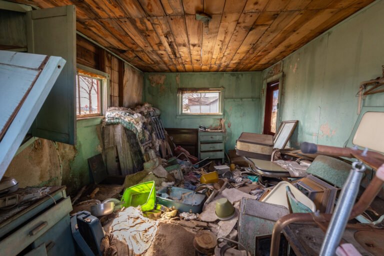Interior of an abandoned, cluttered room with debris, old furniture, and peeling walls.