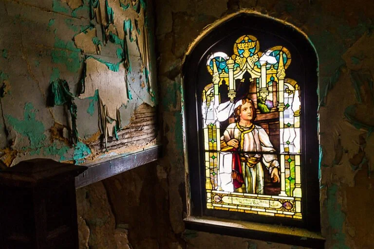 Colorful stained glass window depicting a young boy holding a staff in a dilapidated building with peeling paint and exposed stone walls.