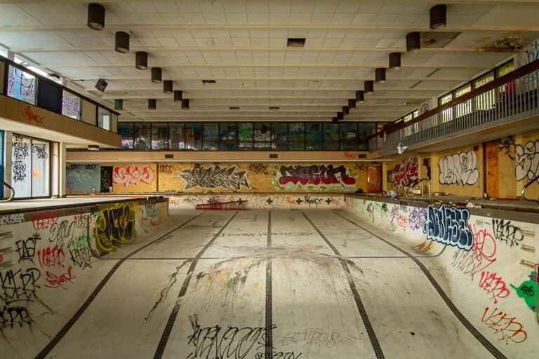 Indoor empty swimming pool with graffiti on walls and pool sides.