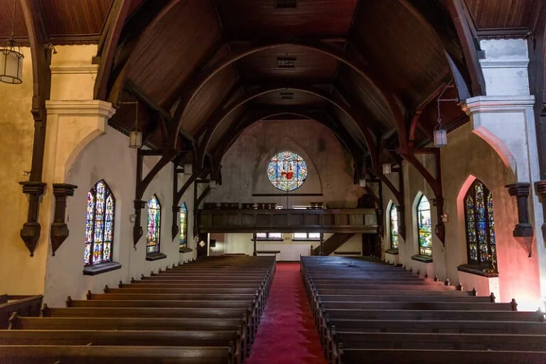 Interior of a church with wooden pews, stained glass windows along the side walls, and a circular stained glass window at the front near the altar.