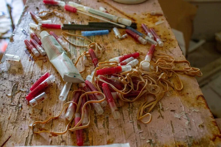 A cluttered wooden table with used syringes, rubber bands, and medical tubing.