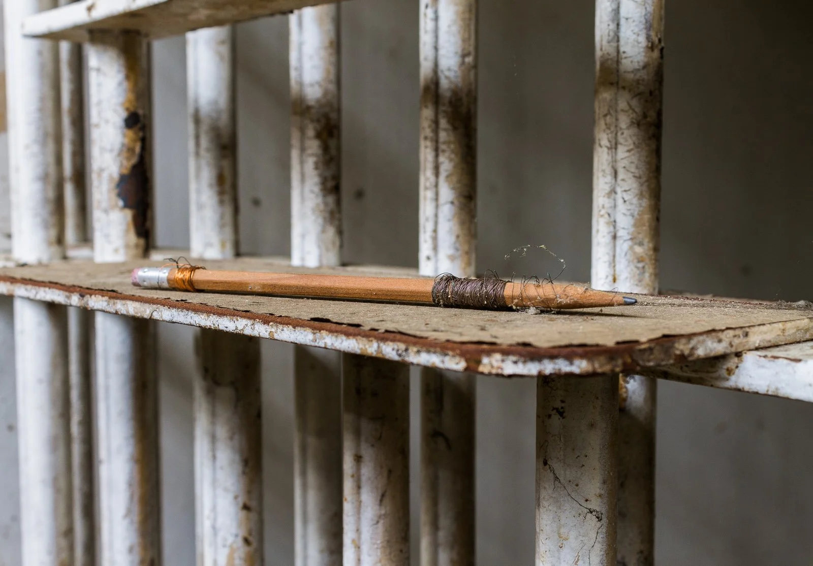 An old, rusted metal cage with a worn-out wooden pencil lying on a chipped wooden shelf inside.
