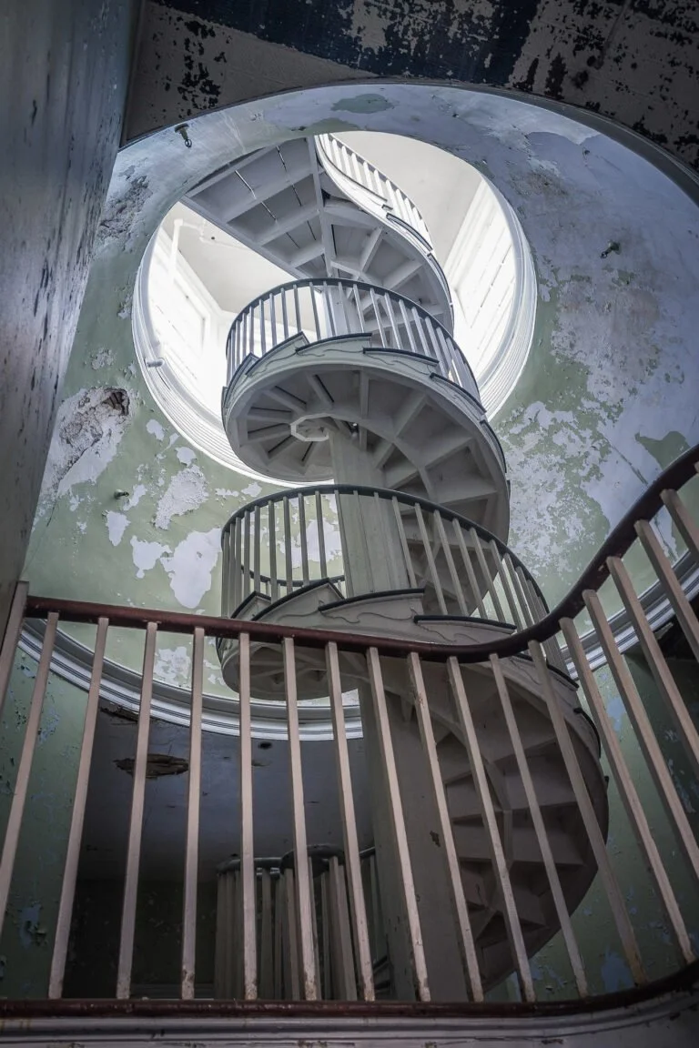 Spiral staircase inside an old, deteriorating building with peeling paint on the walls.