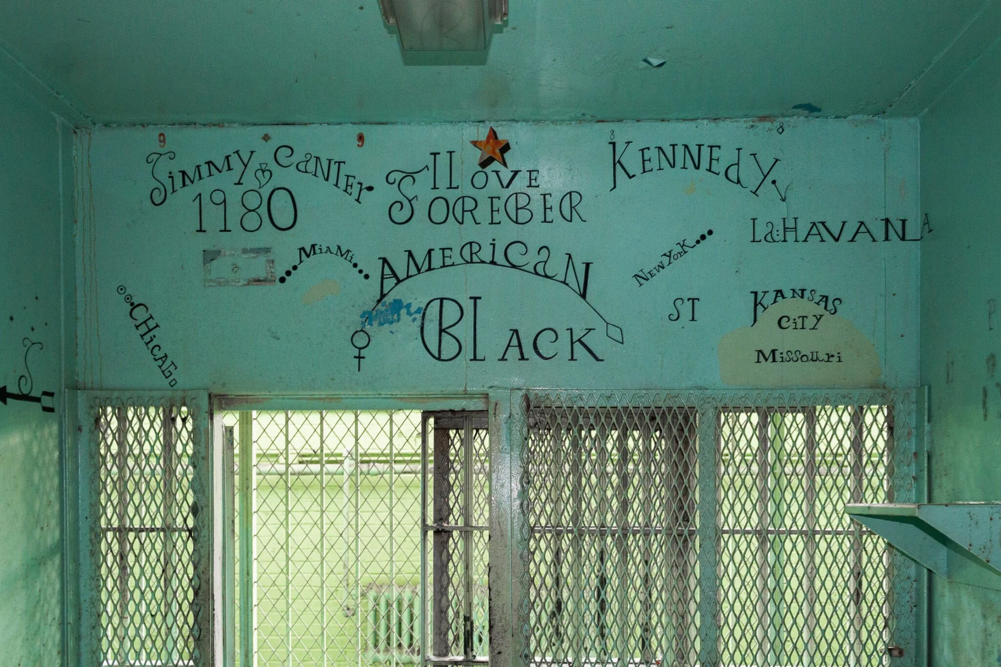 Inside view of a green painted room with painted words and drawings on the walls, including a star and various writings in black ink.