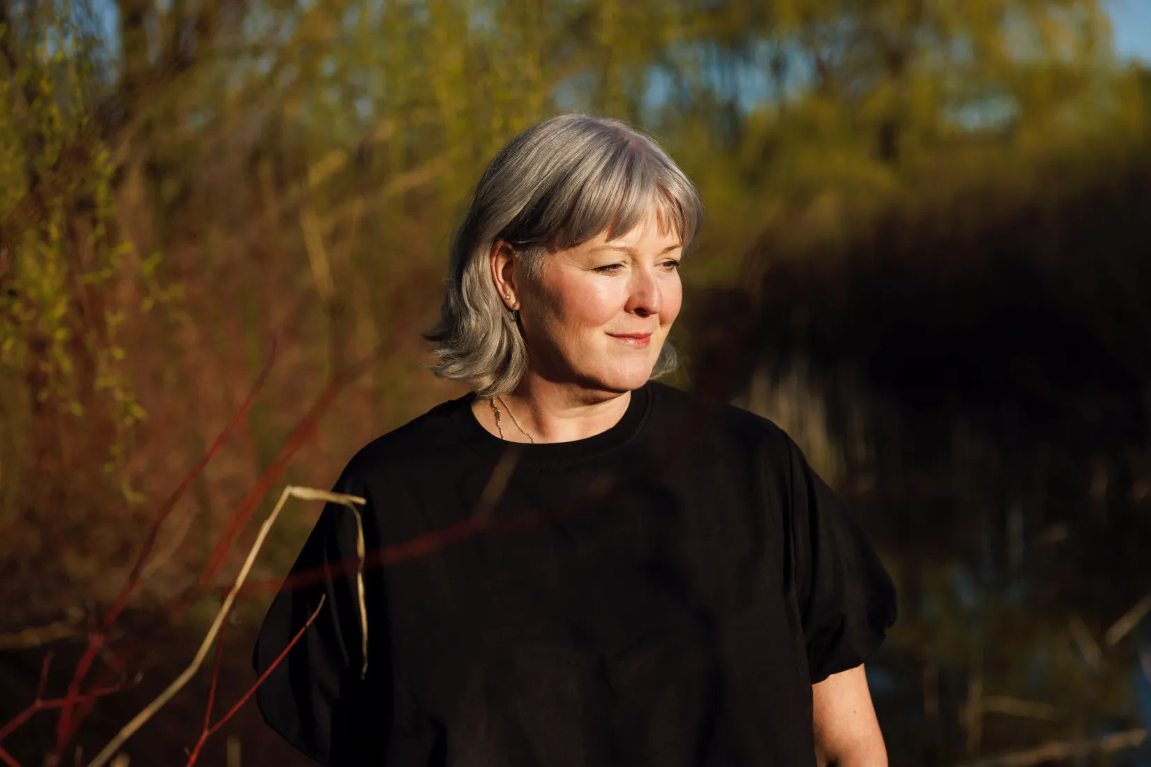 The author Alison Gadsby with evening light falling across her face with a scene of nature in autumn colours blurred behind her