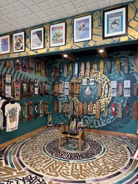 Wall display of skateboards and framed posters in a skate shop with a decorative circular patterned floor.