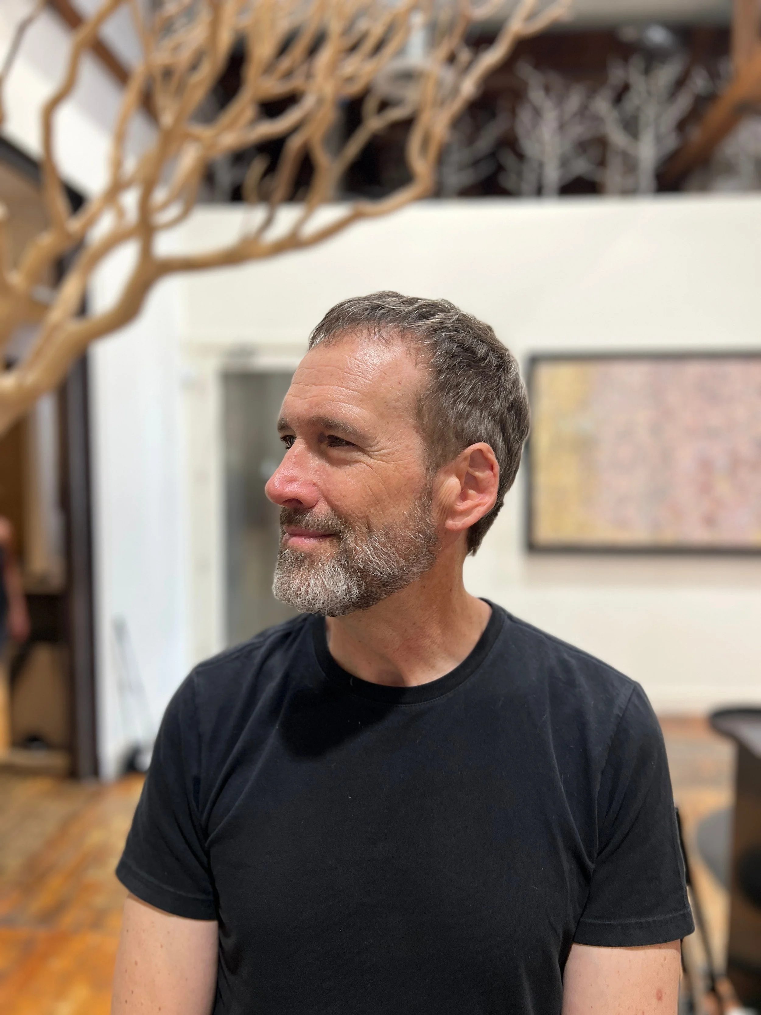 Breton Buckley, gray hair and beard, in a black shirt, looking to his right.