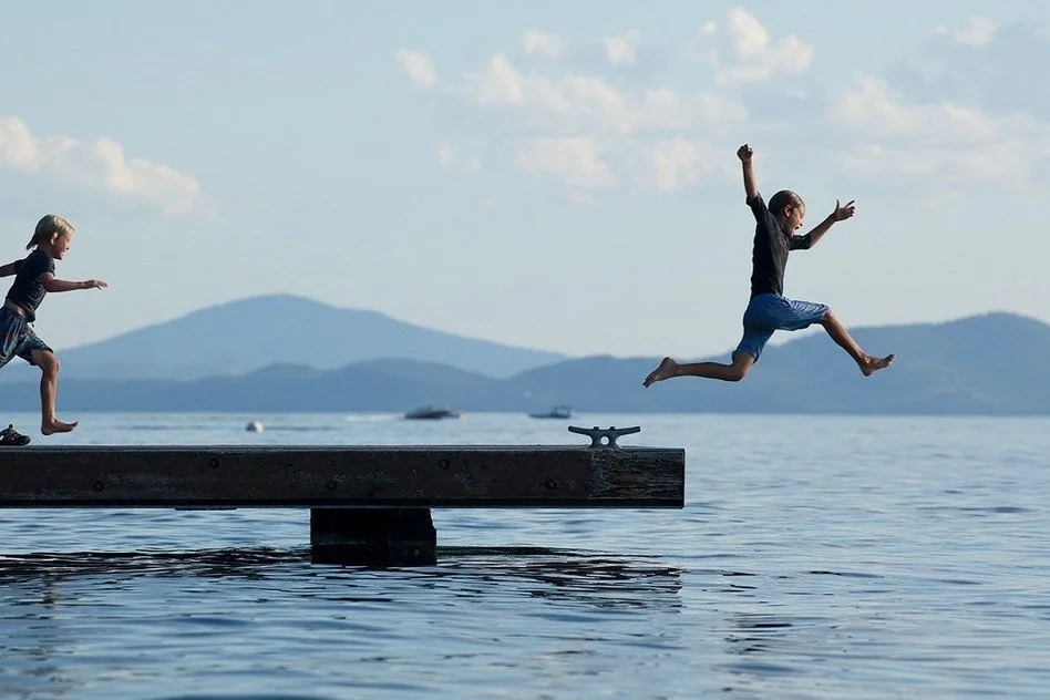 Children jumping off a dock into a mountain lake