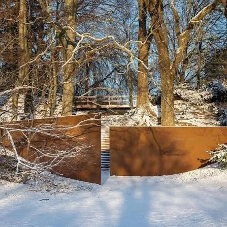 A weathering-steel sculpture set into a snowy wooded slope