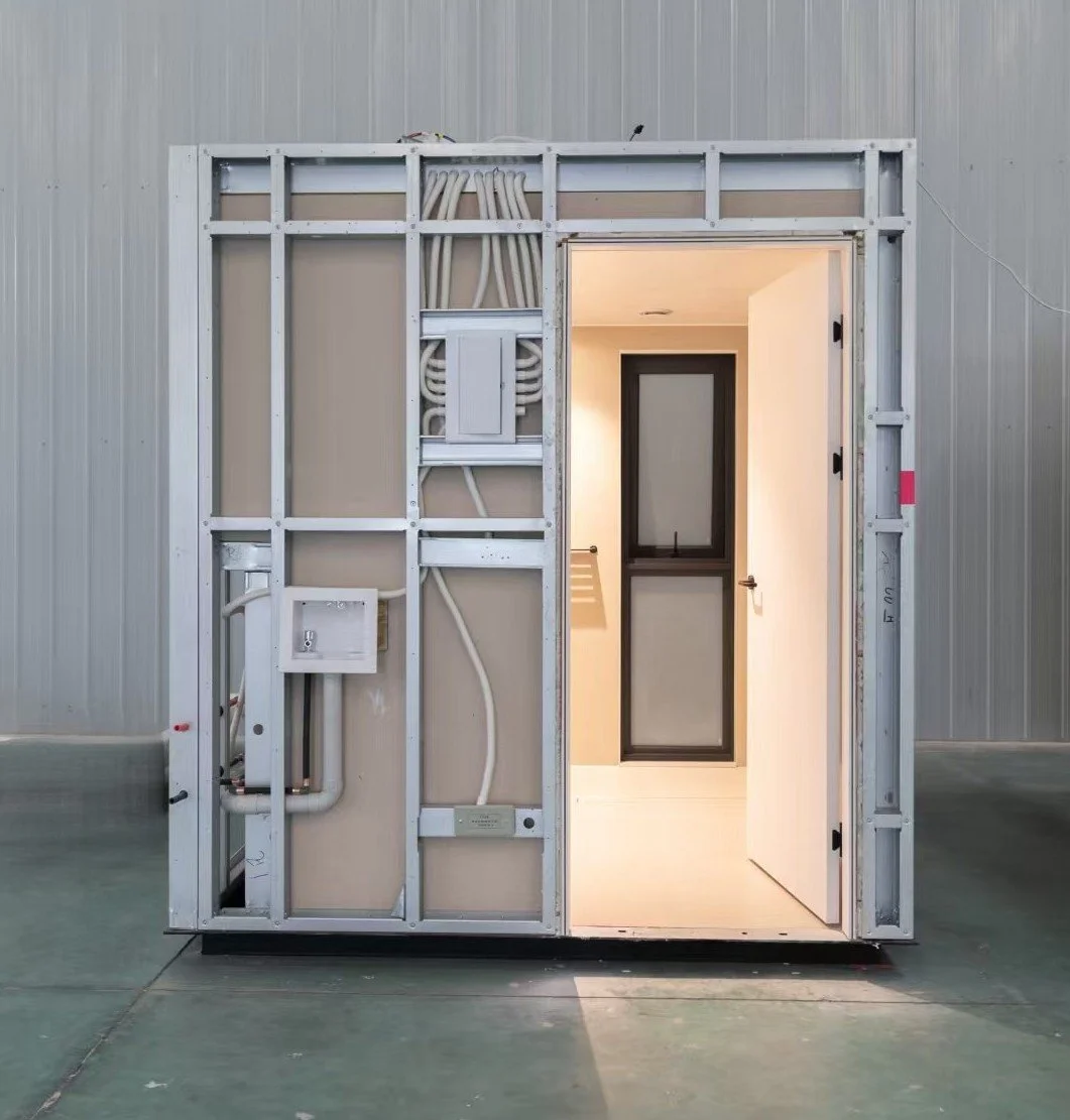 A steel-framed modular pod with its door open, plumbing and wiring on the outside wall