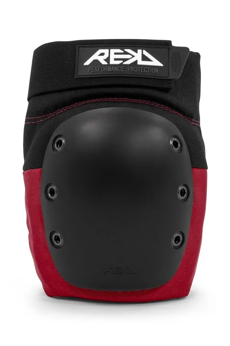A protective knee pad or sports pad with a black hard shell, red fabric on the bottom, a black strap with a logo that says 'REKD Performance Protection', and multiple rivets or fasteners.