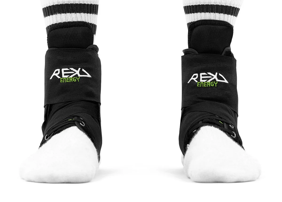 Pair of ski boots with white socks, black boots with green and white "REKD ENERGY" logo, on a white background.