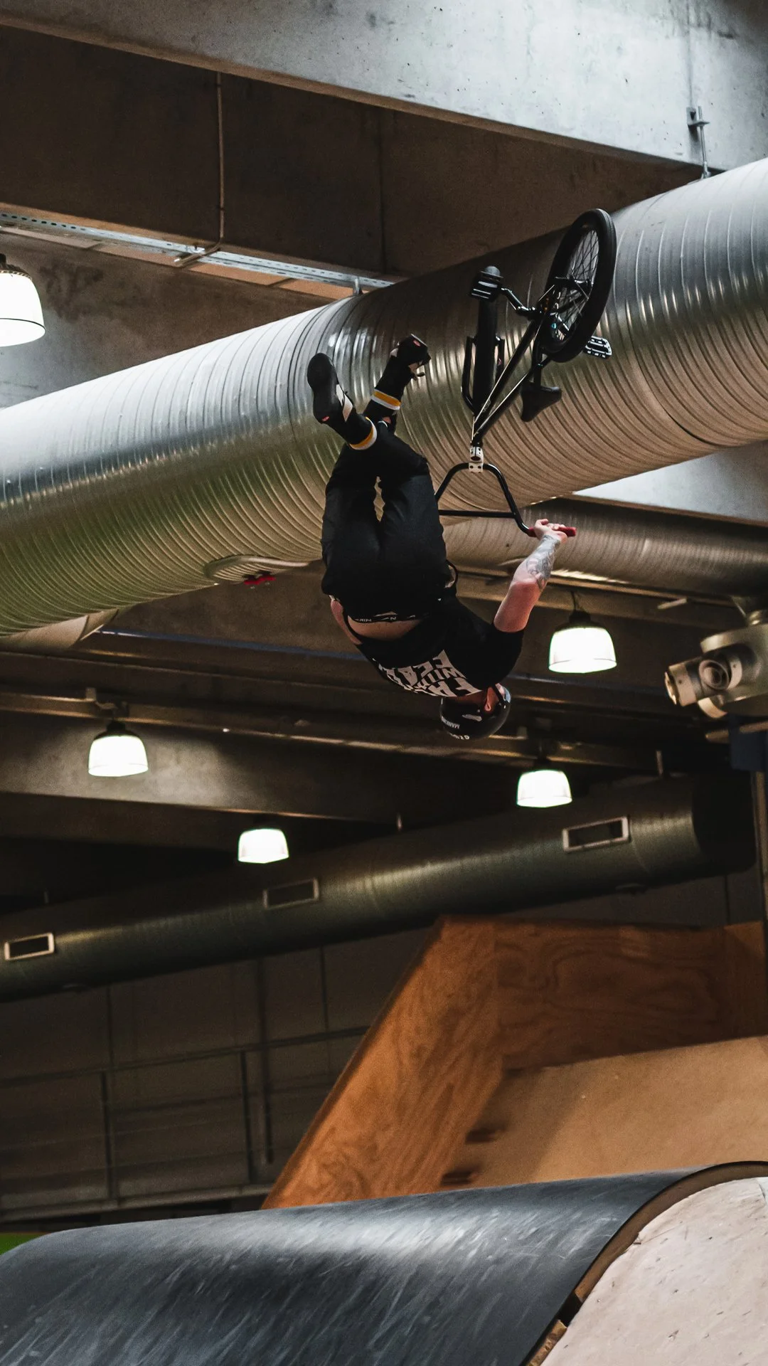 A person doing an upside-down trick on a BMX bike at an indoor skatepark.
