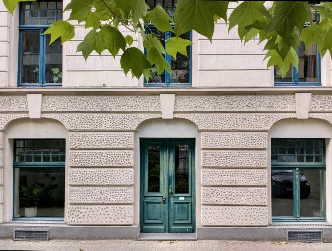 Ansicht eines Gebäudes mit grauem Massivholz-Tür und vier Fenstern, von denen zwei im Erdgeschoss und zwei im oberen Stockwerk, umgeben von grünen Blättern
