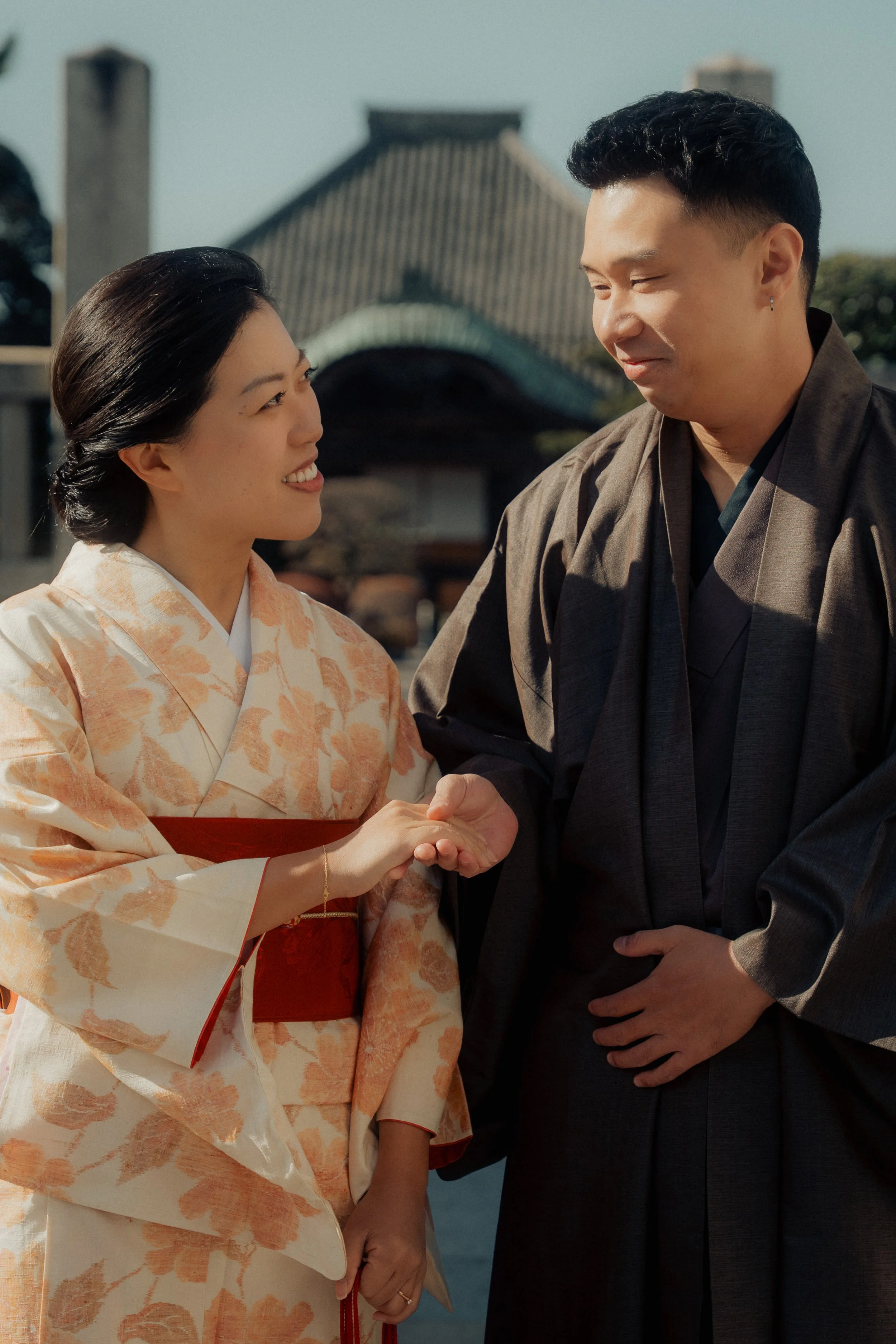 A woman in a peach and cream kimono shaking hands with a man in a dark traditional robe.