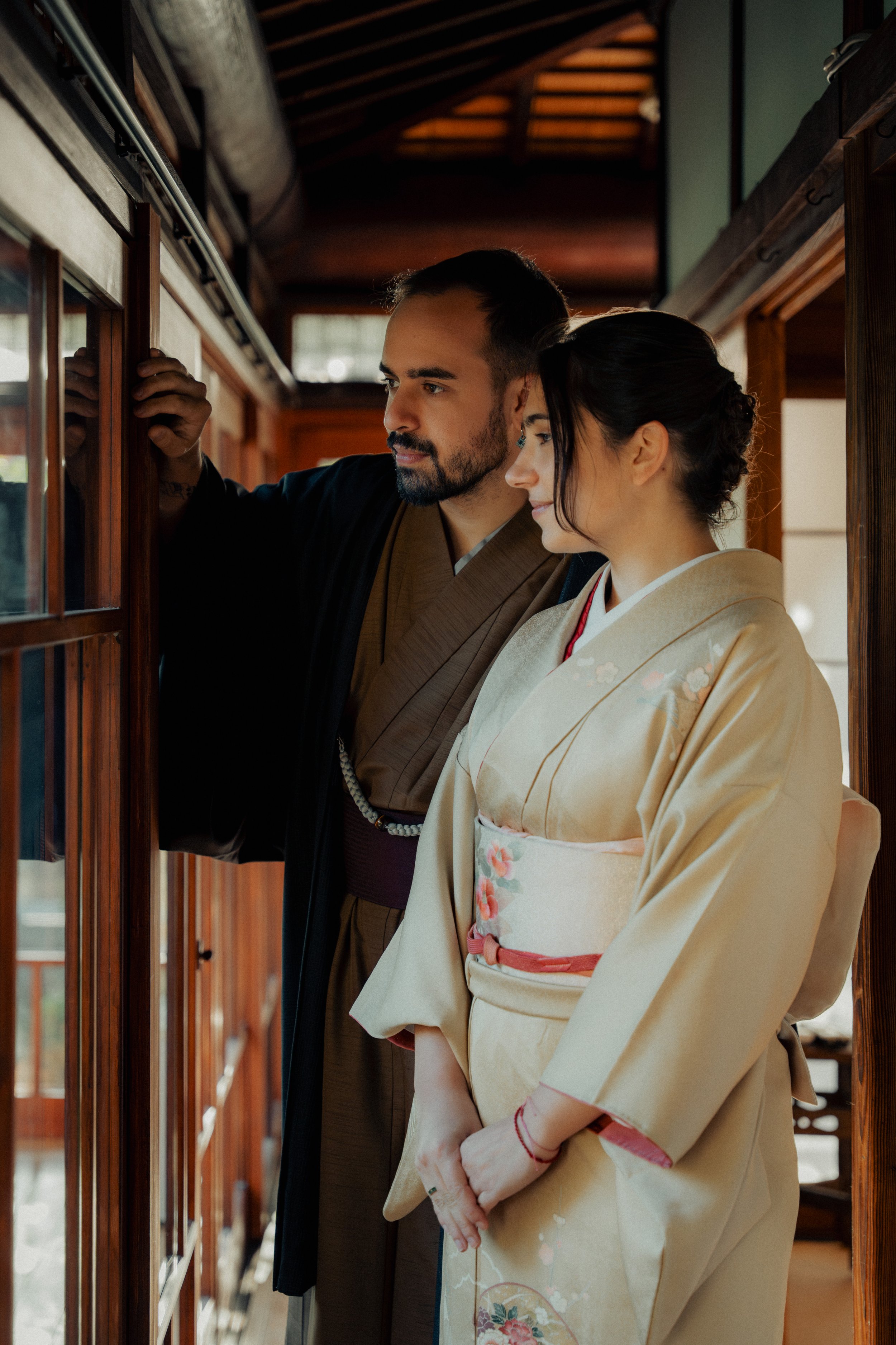 A man and woman wearing traditional Japanese kimonos looking at items inside a wooden display case in a Japanese-style building with a wooden ceiling.