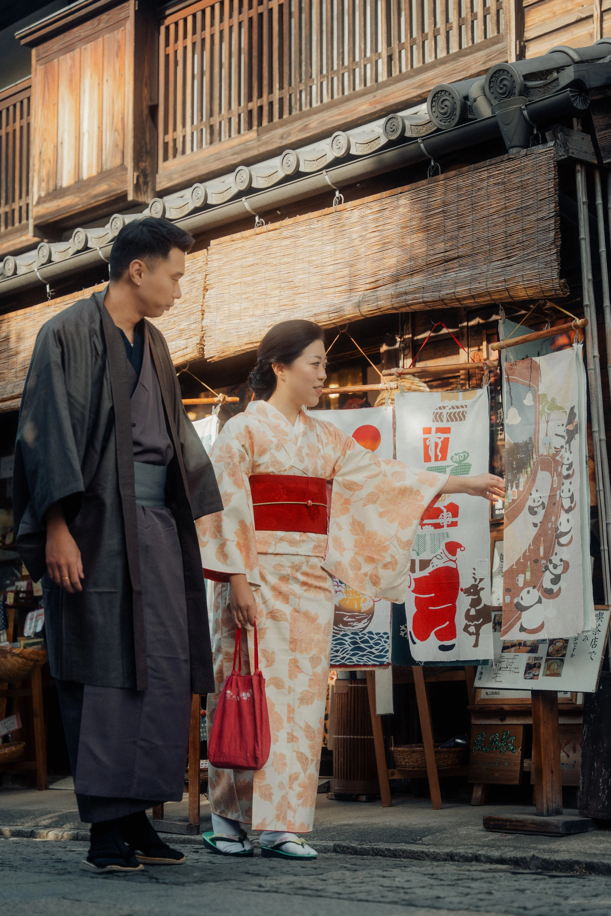 A man and woman dressed in traditional Japanese clothing walking past a street stall with colorful fabric banners displaying Japanese art and characters.
